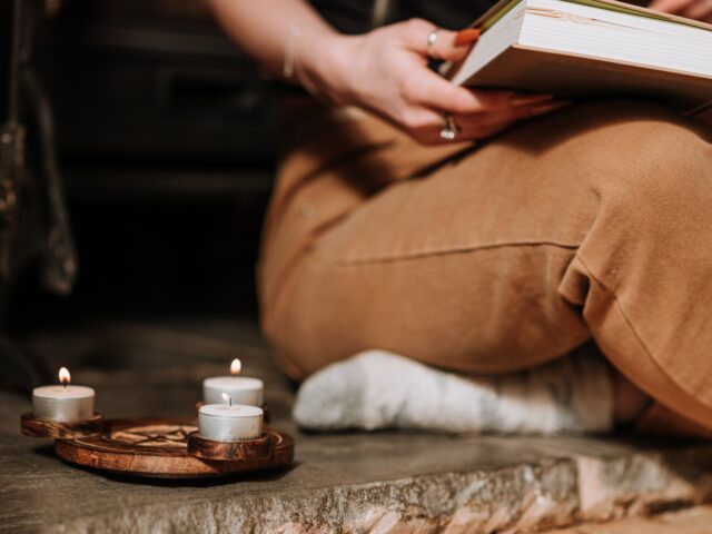mujer sentada junto a unas velas con un libro en sus piernas escribiendo para celebrar el equinoccio de otoño